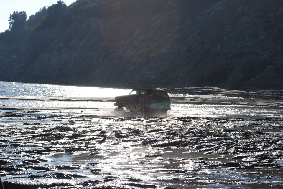 SUV driving through a muddy, watery area with a hill in the background