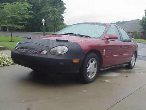 1998 Ford Taurus - Red 1998 Ford Taurus sedan is parked outside on a wet driveway, partially covered.