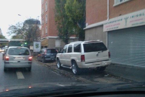 1991 Ford Crown Victoria - White Cadillac Escalade parked on a street next to a building with a closed garage door.