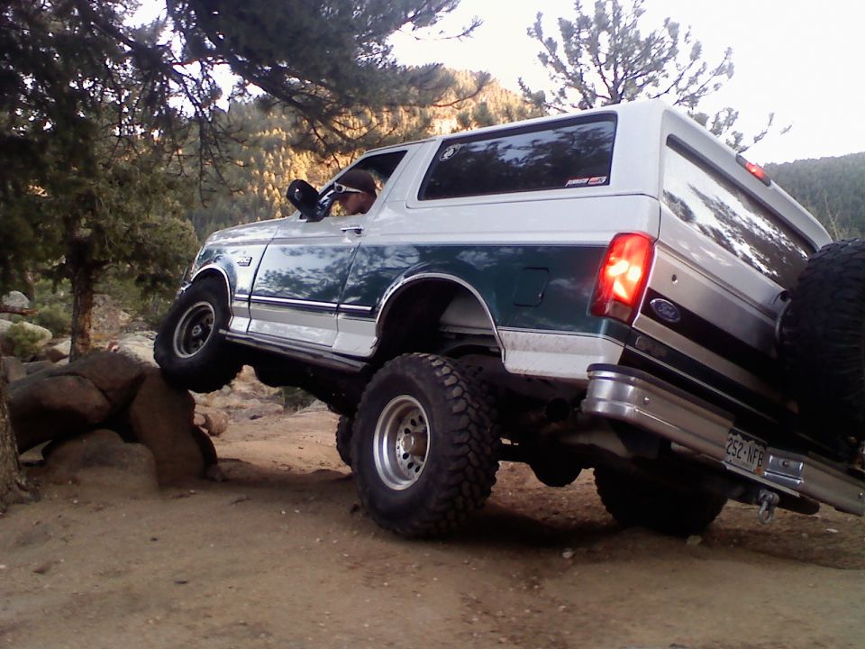 White and green Ford Bronco climbing over rocks on a dirt trail
