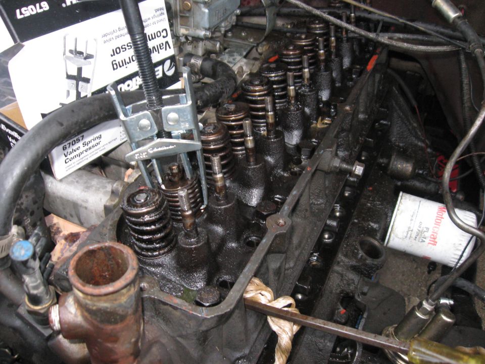 Rented a valve spring compressor that can be used without removing the head.
Since I don't have an air compressor, I had to use the old trick of filling the combustion chamber with rope, or else the valves would fall inside.  The screwdriver helped for some leverage if I needed to lift the valve all the way up.