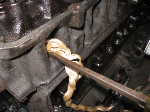 1981 Ford Bronco - Close-up of a light-colored braided rope-style rear main seal being twisted around a steel bar against the oily engine block. The open lift…