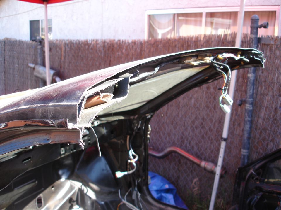 Black car body shell with roof cut off, showing ragged cut metal edges and exposed wiring in a backyard
