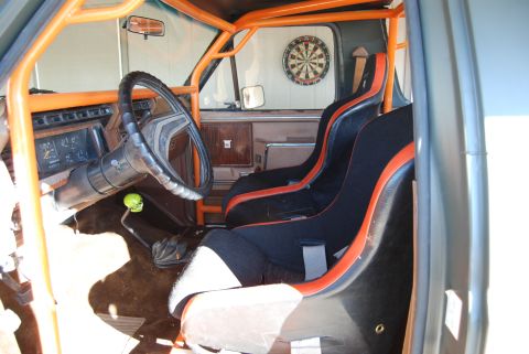 1982 Ford Bronco - The interior of a truck features racing seats and an orange roll cage, with a dartboard visible on the wall.