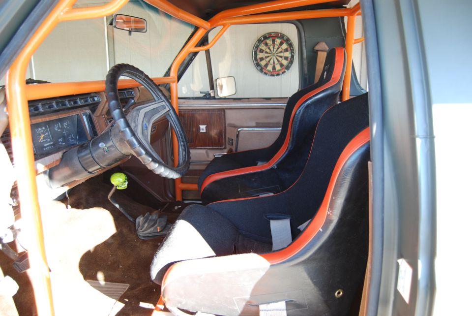 Interior of a truck with racing seats, orange roll cage, and a skull shifter