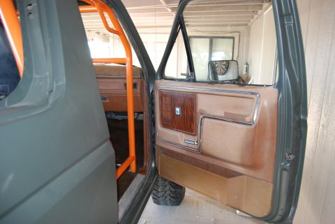 1982 Ford Bronco - The interior of a 1982 Ford Bronco shows a door panel with wood trim and an orange roll cage visible inside.