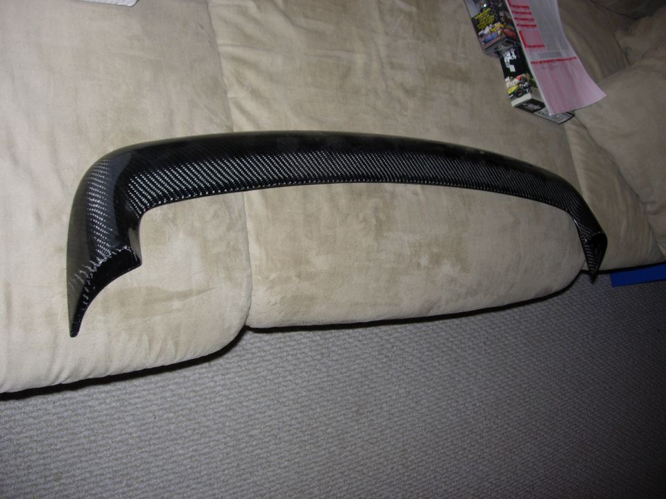 Carbon fiber rear spoiler lip resting on a tan couch cushion indoors