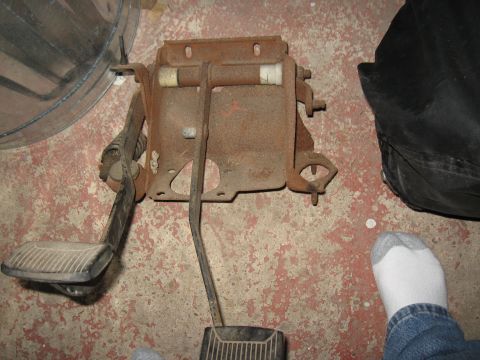 1994 Ford Bronco - A rusty clutch pedal assembly with two pedals is shown on a concrete floor.