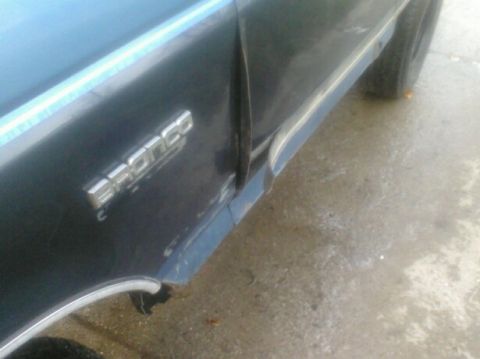 1989 Ford Bronco - Close-up of a dark blue vehicle's side panel, showing the chrome 'Bronco' emblem.