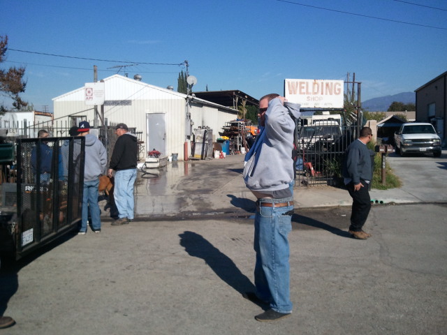 People gathered outside a welding shop with a white truck and a trailer