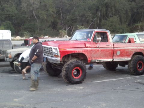 1979 Ford Bronco - A lifted red pickup truck with custom wheels is parked in a lot next to another vehicle.
