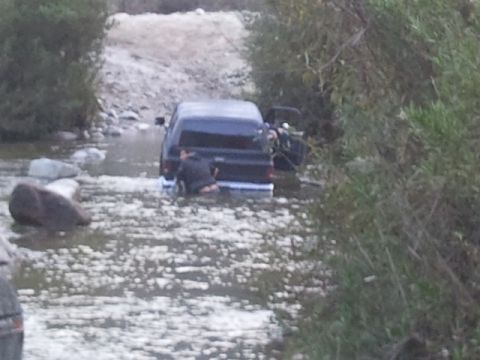 1979 Ford Bronco - A black 1978 Ford Bronco is stuck in a stream, with a person visible near the rear bumper.