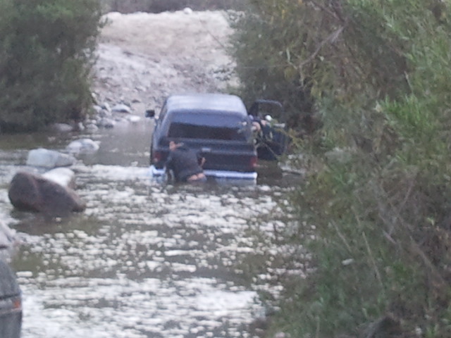 Black 1978 Ford Bronco partially submerged in a rocky stream with its rear facing the camera
