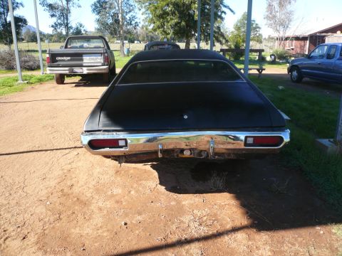 1975 Ford Ranchero - Rear view of a black 1972 Ford Ranchero with a dented chrome bumper, parked outdoors.