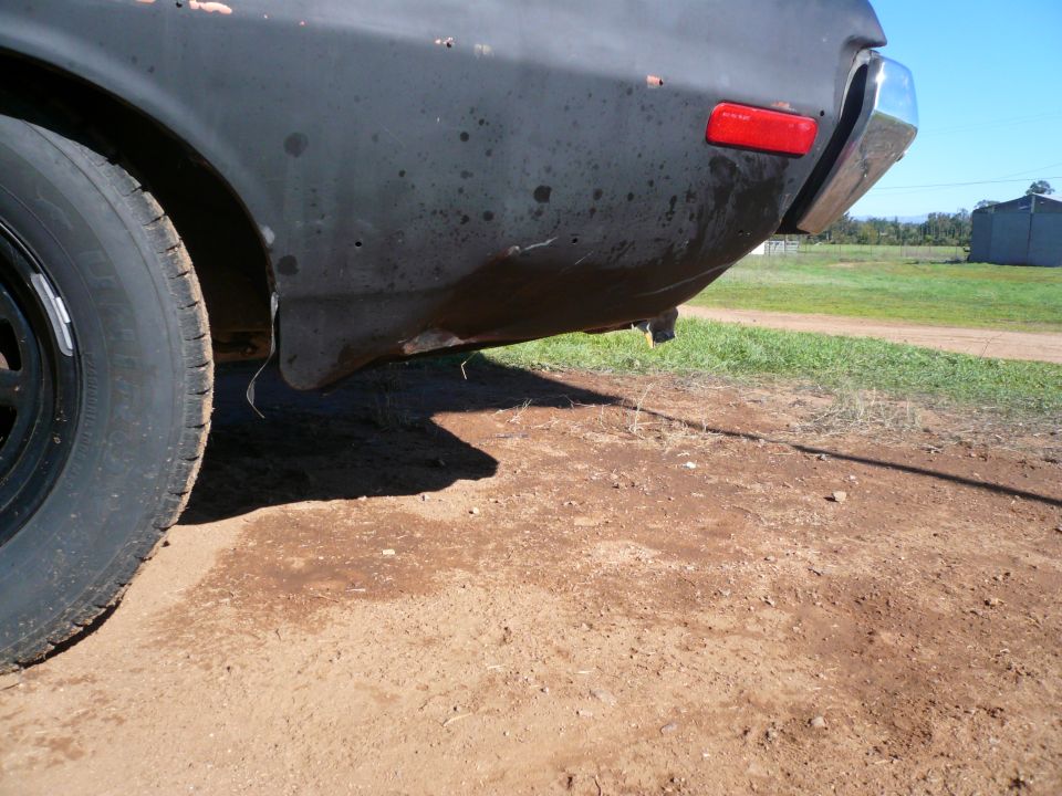 Black car's rear fender and chrome bumper with a red taillight, seen from a low rear angle