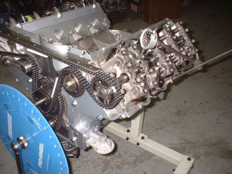 1965 Shelby Cobra - Engine assembly on a stand, showing timing components and a dial indicator for measurement.