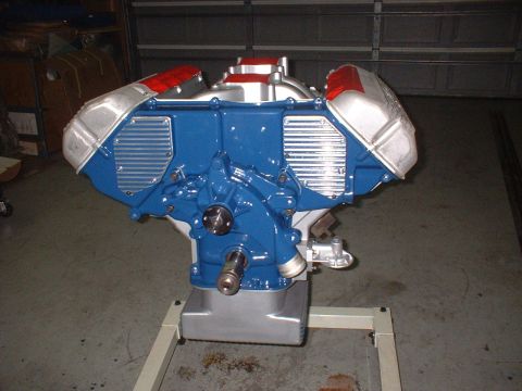 1965 Shelby Cobra - A V8 engine, painted blue with silver and red accents, is displayed on a metal stand in a garage.
