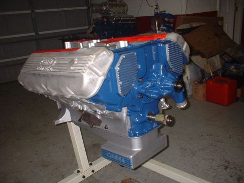 1965 Shelby Cobra - A Ford 427 SOHC engine, painted blue and silver, is displayed on a stand in a garage setting.