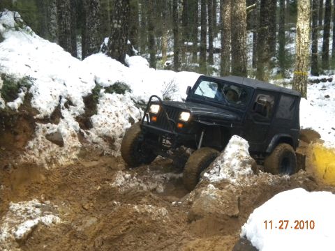 2005 Jeep Wrangler - A black Jeep Wrangler tackles a challenging off-road course with mud and snow.