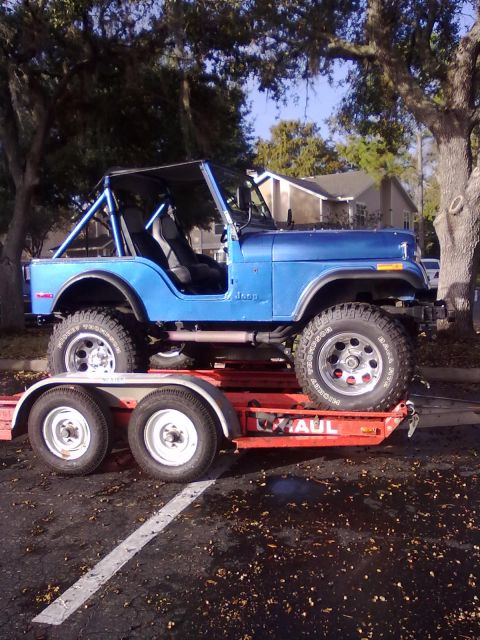 1978 Jeep CJ5 - A blue Jeep CJ is loaded onto a red trailer, ready for transport.