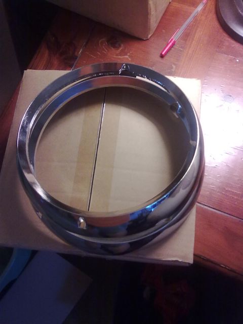 1978 Jeep CJ5 - A chrome headlight bezel rests on a cardboard box on a wooden surface.