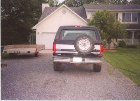 1996 Ford Bronco - Straight-on rear view of a black full-size Ford Bronco with hardtop and silver tailgate stripe parked on a gravel driveway, carrying a swin…