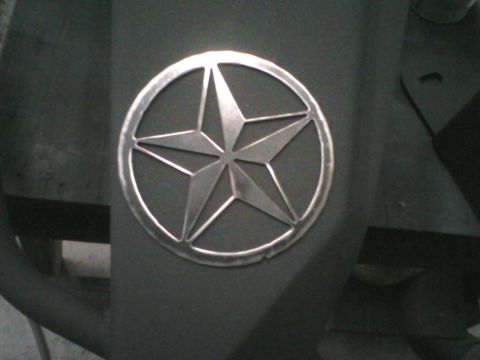 1993 Ford Bronco - Close-up of a bare metal five-point nautical star emblem inside a welded ring, mounted on a flat gray-primered panel. The faceted star and…