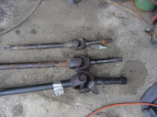 Three front axle shafts with U-joints laid on shop floor to compare sizes