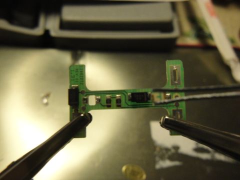 2003 Ford Crown Victoria - Close-up of a circuit board being held with tweezers, showing some legible text.