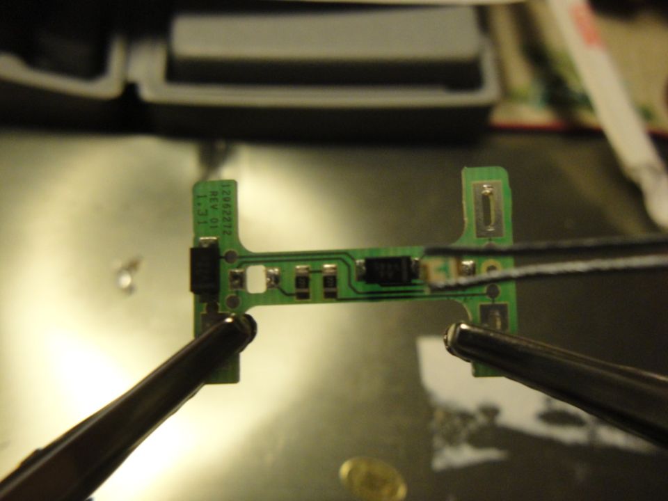 Circuit board held by tweezers, with text '12892212 REV 01 1.31' visible