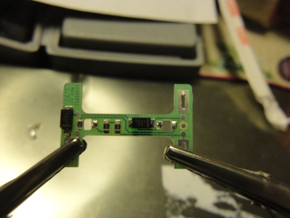 Circuit board held by tweezers, with small electronic components soldered on