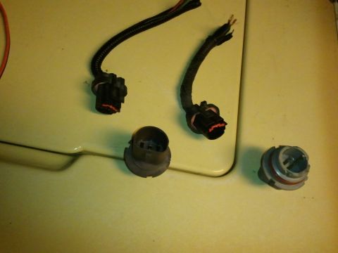 2003 Ford Crown Victoria - Several headlight harness connectors and bulbs are laid out on a yellow surface, likely for repair or replacement.