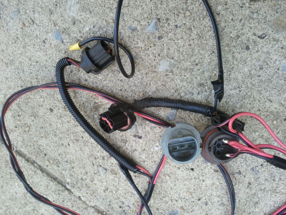 Automotive headlight wiring harness with two connectors and two bulb sockets, lying on concrete