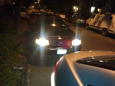 2003 Ford Crown Victoria - A 2003 Ford Crown Victoria is parked on a residential street at night with its headlights illuminated.