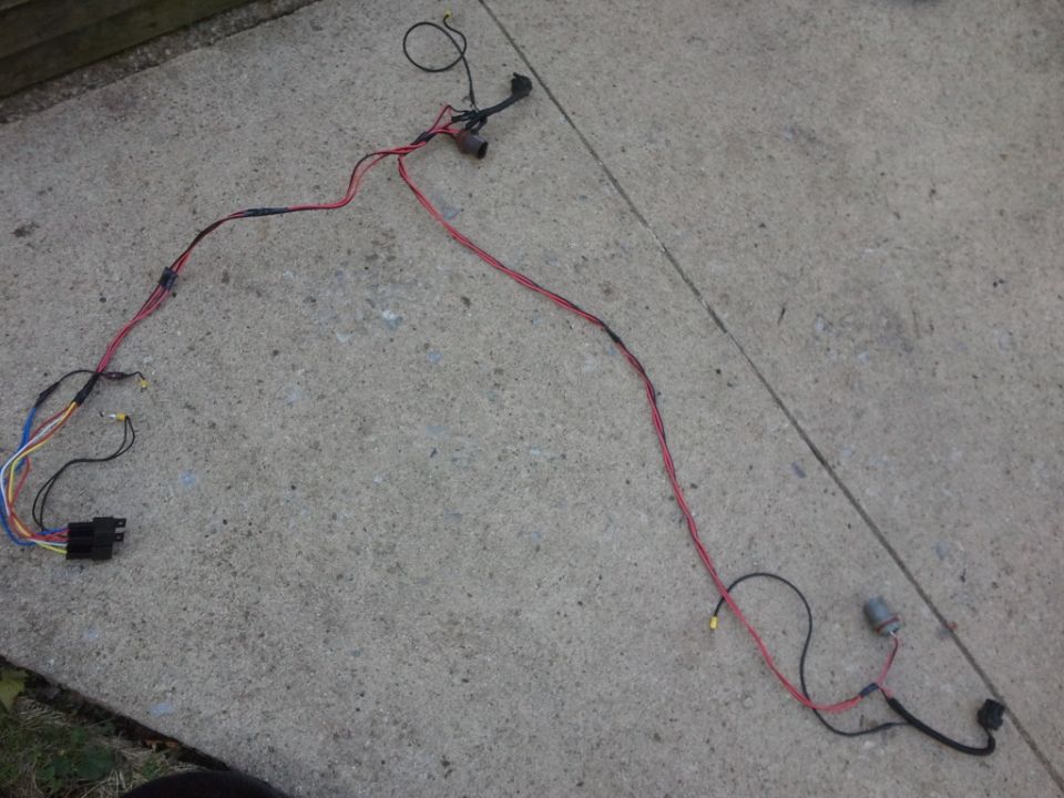 Automotive wiring harness with red and black wires, connectors, and a black plastic housing, laid out on concrete