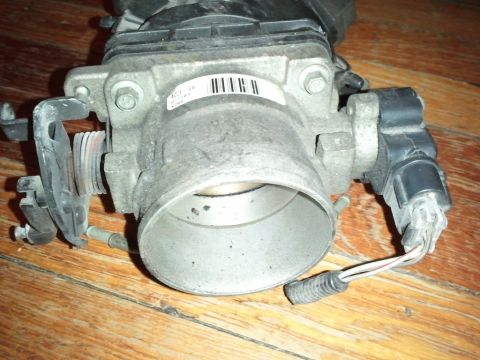 2003 Ford Crown Victoria - A throttle body part is shown on a wooden surface. It has a label with a barcode and some text.