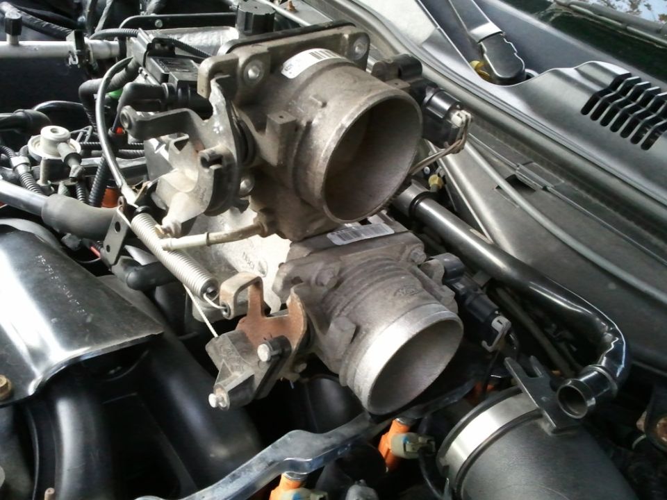 engine throttle body assembly with two connected units and various hoses and wires