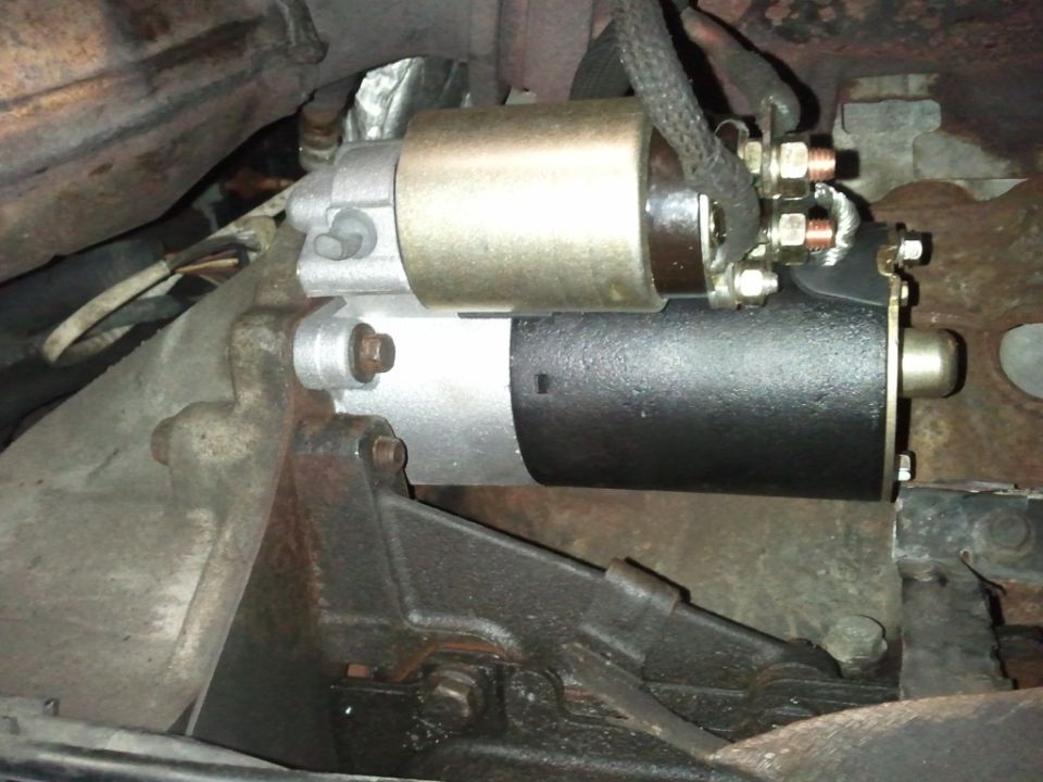 Close-up of a vehicle's starter motor, showing electrical connections and mounting bracket