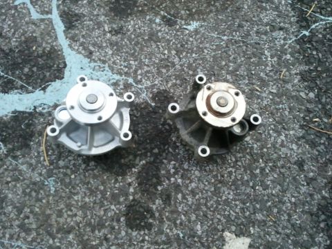2003 Ford Crown Victoria - A new water pump is compared to an older, used one on a paved surface.