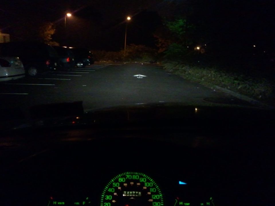 Car dashboard with illuminated speedometer and parking lot at night