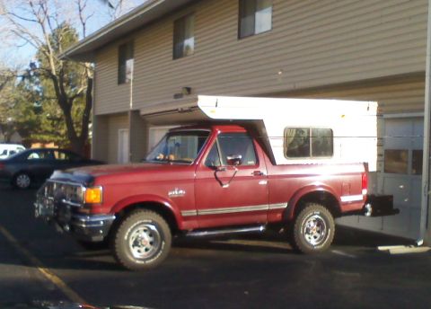 1995 Ford Bronco - This red 1995 Ford Bronco is equipped with a white camper shell, seen from a three-quarter front perspective.