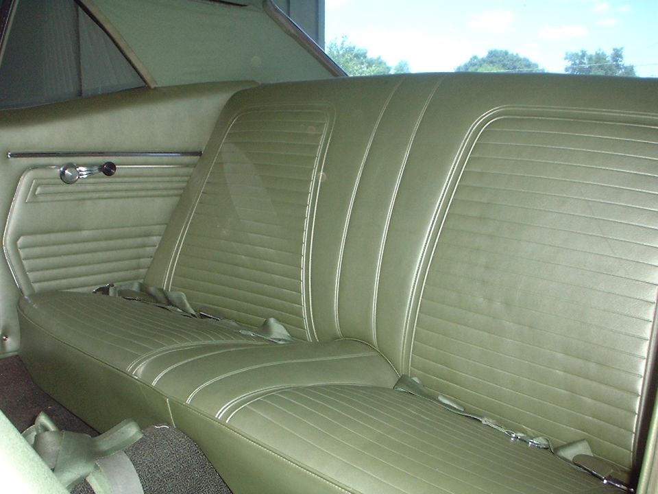 Green vinyl rear car seat with lap belts, showing ribbed upholstery and door panel detail