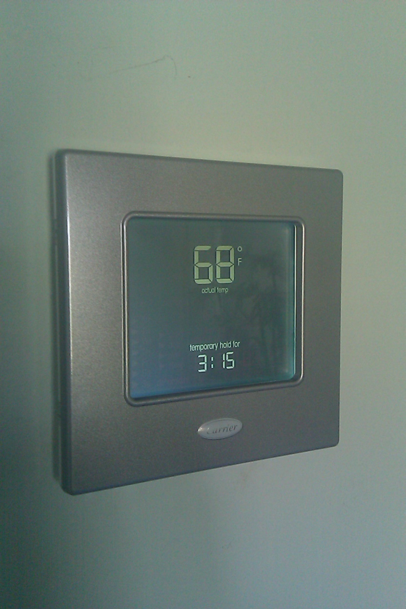 Gray digital thermostat on a light-colored wall, displaying 68 degrees