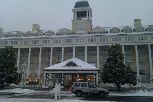 Silver Jeep Grand Cherokee parked in front of a large hotel with a clock tower, during a snowfall