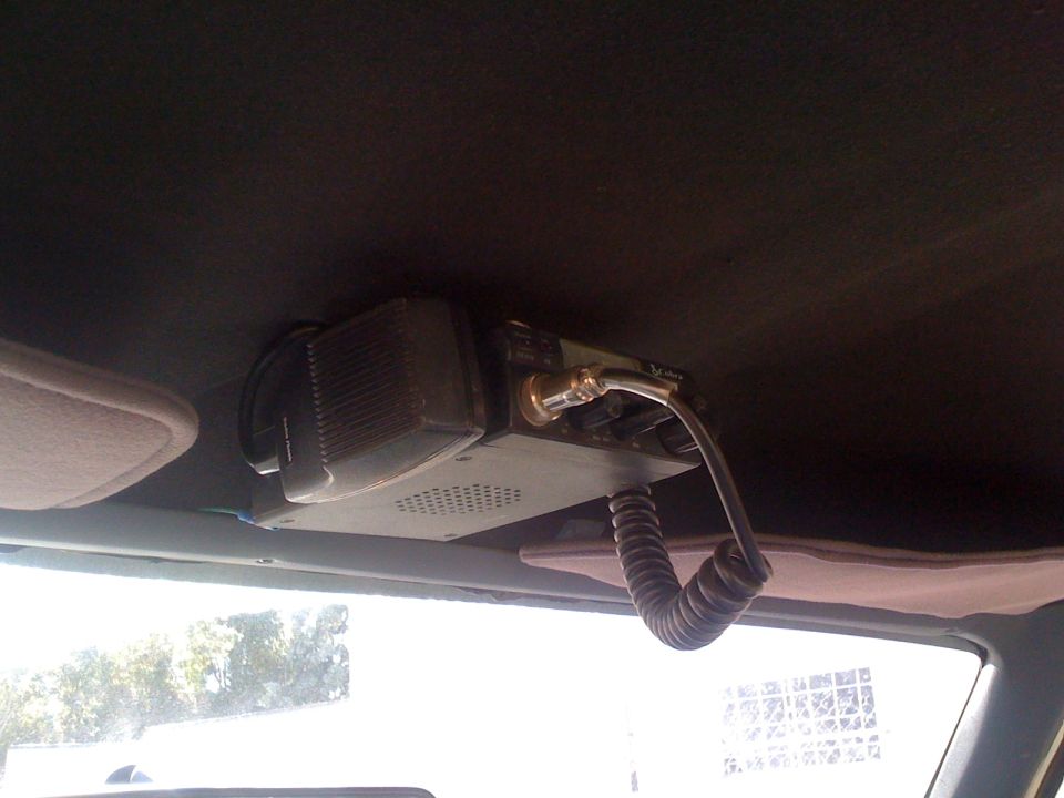CB radio with coiled cord mounted on dark headliner, sun visors visible