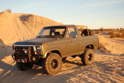 1982 Ford Bronco - A lifted Ford Bronco is parked on a sandy incline under a clear sky.