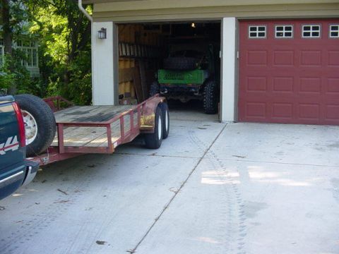1992 Ford Bronco - A trailer is hitched to a pickup truck, parked outside a garage where a green off-road vehicle is visible.