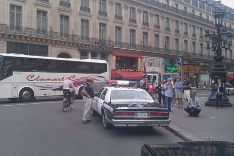 1991 Ford LTD Crown Victoria - A police car with emergency lights is parked on a street next to a bus and several pedestrians.