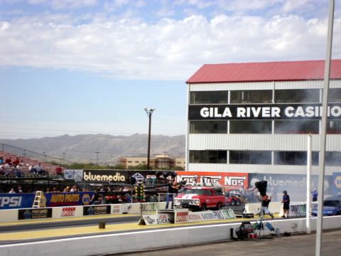 1979 Ford Bronco - A red pickup truck is staged at a drag strip, with spectators in the stands and a casino building behind the track.