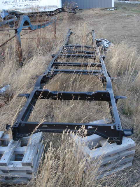 1977 Ford F-150 - A bare truck frame rests on pallets in a grassy, outdoor area. The frame is black and appears to be for a pickup truck.